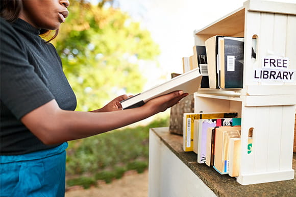 A woman selecting a book from a free little library